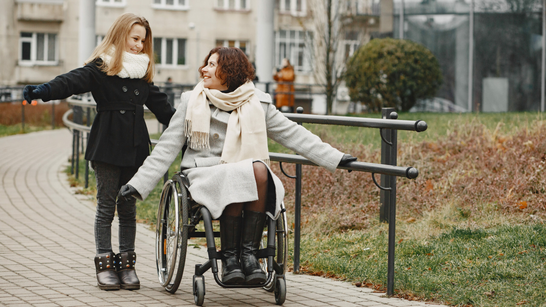 Disabled woman in wheelchair with daughter. Family walking outside at park.