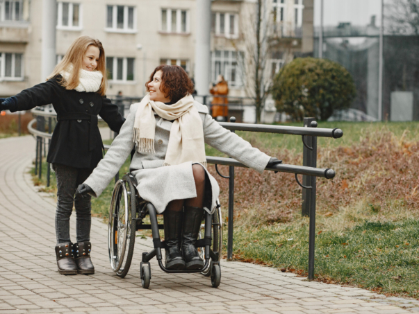 Disabled woman in wheelchair with daughter. Family walking outside at park.
